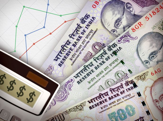 Three money bills in front of sheet of paper with a graph on it symbolizing economic relationships.